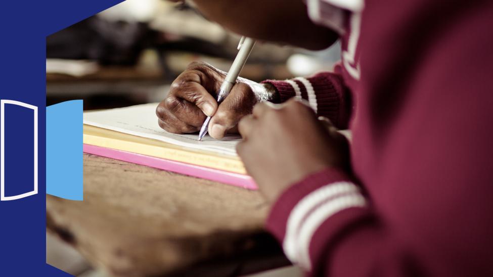 Learner at school desk writing on pad